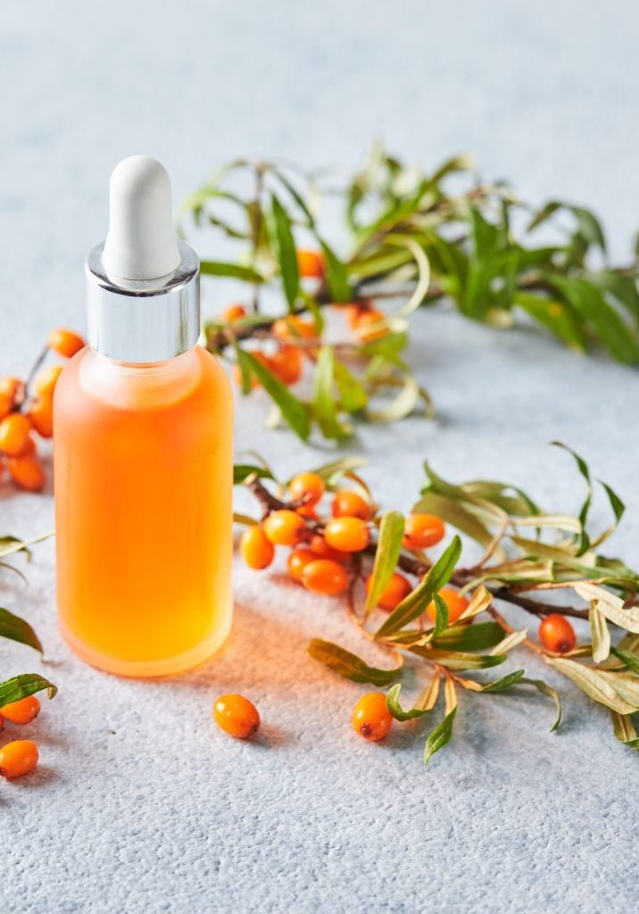 Glass bottle with sea buckthorn oil, berries and branches of sea buckthorn on light background. Self-care, cosmetics, beauty practices, self-care concept.